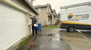Perfection Garage Door technician measuring a garage door opening with a tape measure at a Renton, WA home before a replacement, company van in the driveway